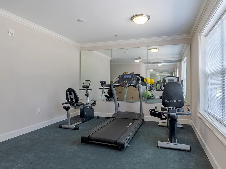 Well-lit fitness center equipped with treadmill, stationary bike, and mirrored wall designed for resident wellness at Snowden Senior Apartments.