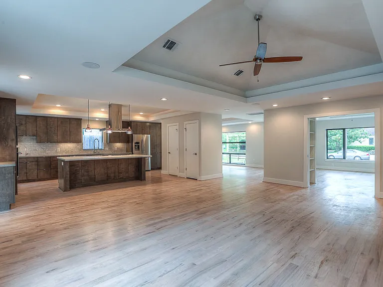Open-concept great room flowing into the chef's kitchen _ dramatic tray ceiling, walnut-stained cabinets, large island, and stainless appliances