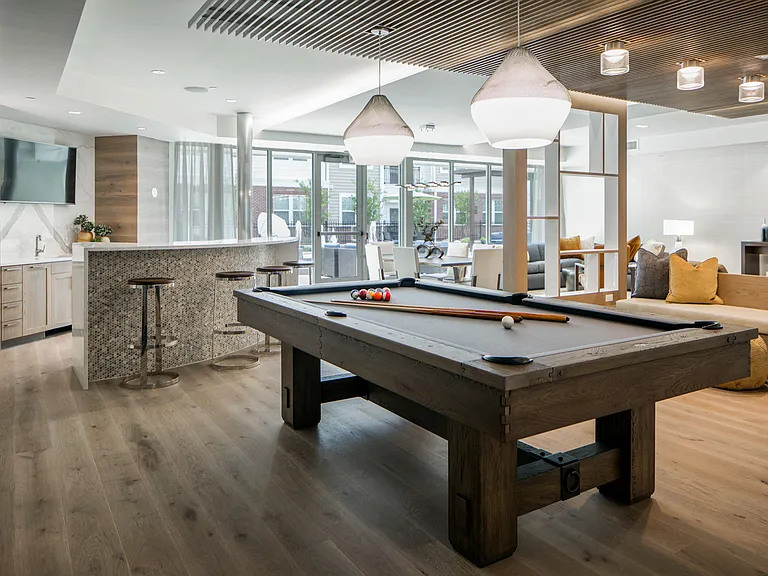 Community living room with plenty of comfortable seating, bar area for socializing, kitchen amenities, billiards table, business area with available computers and TV