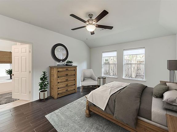 The Primary Bedroom Suite is located separately from the other 3 Bedrooms for privacy. Wood-like tile floors, recent ceiling fan, and recent solar shades on windows. Open door leads to impressive Primary Bathroom. Windows overlook backyard. PHOTO VIR