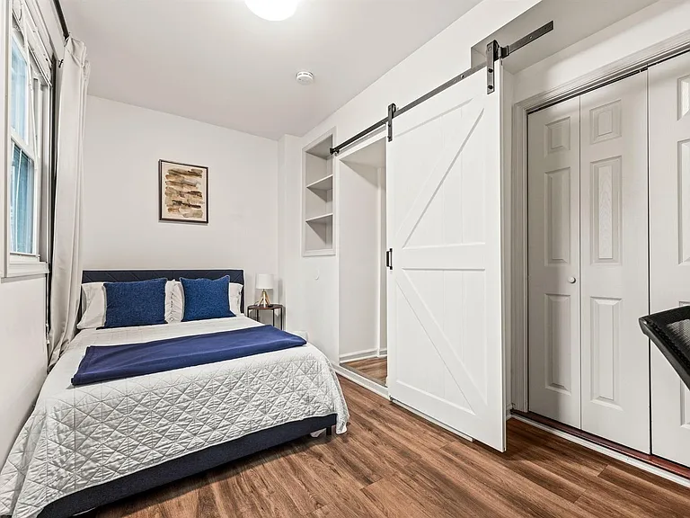Bedroom with a full-size bed, large window, and hardwood-style floors, plus a barn-door closet and built-in shelving.