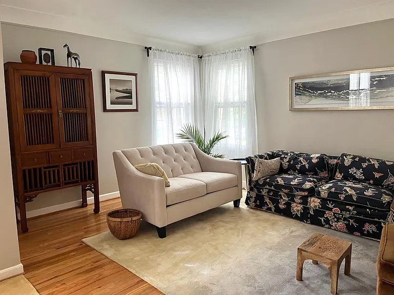 Living room with loveseats, cabinet, area rug and windows for light and ventilation.