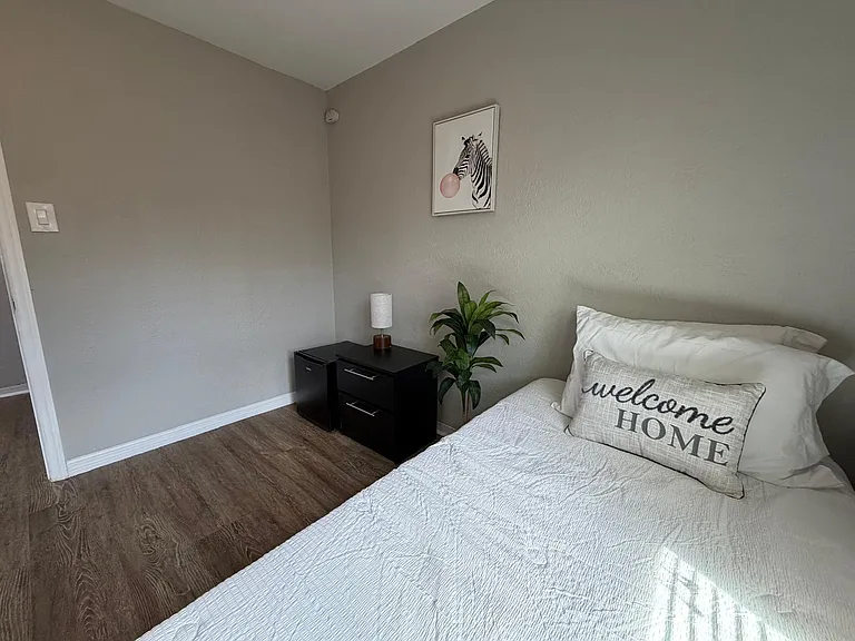 Furnished bedroom with wood-look flooring, a comfortable bed setup, and nightstand storage for everyday essentials.