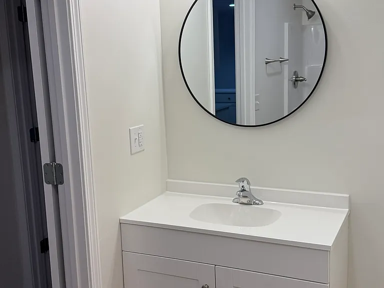 Modern bathroom vanity featuring a clean white cabinet with ample storage, a bright countertop, a contemporary round mirror, a stylish three-light fixture, and coordinated finishes for a fresh, elegant look.
