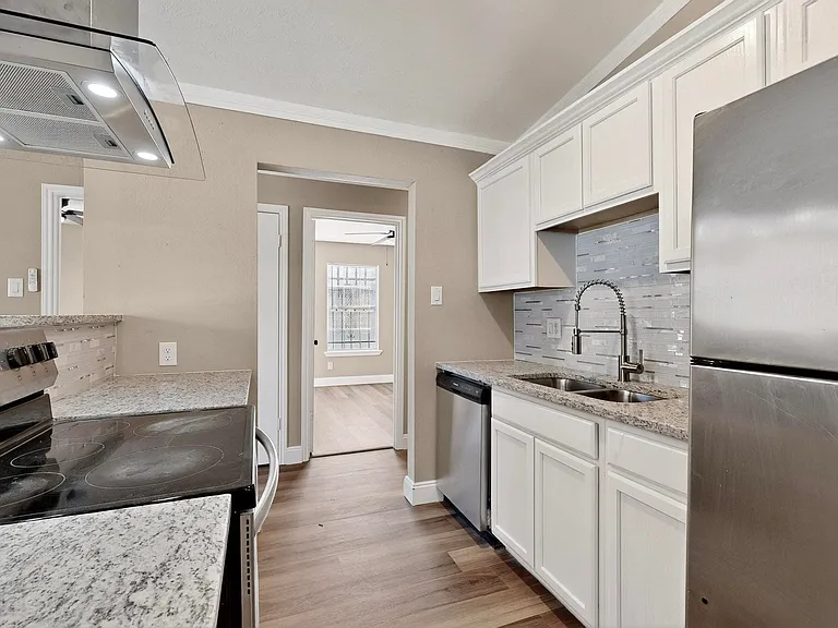 Kitchen featuring stainless steel appliances, exhaust hood, white cabinets, light stone counters, and crown molding