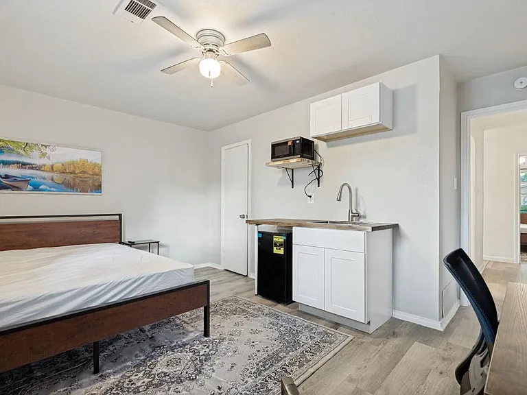 Spacious furnished bedroom with a convenient in-room kitchenette with sink, cabinets, microwave, mini fridge, & ceiling fan.