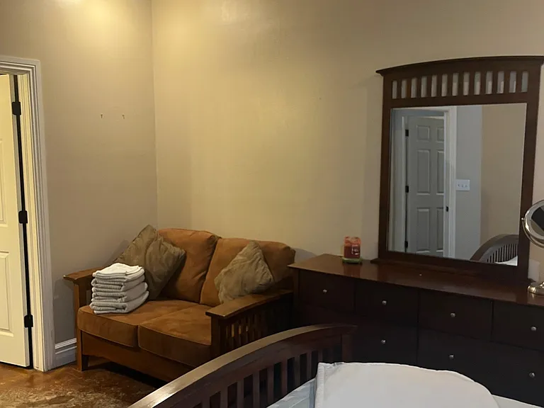 Furnished bedroom featuring a bed, dresser with mirror, and a sitting area, plus ceiling fan and easy access to the hall.