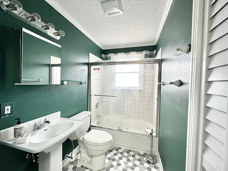 Tub/Shower combination with shower door, specialty tiles, pedestal vanity and storage.