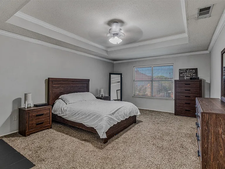 Spacious room featuring a tray ceiling with crown molding, textured carpeting, and a window with blinds