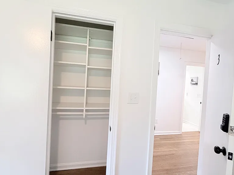 Entry area with an open storage closet and wood-style flooring, providing convenient organization near the room access.