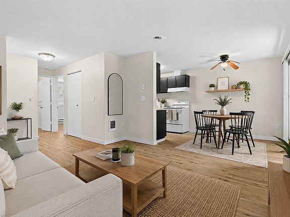 Staged 1-Bedroom Deluxe with an open-concept living and dining area with wood-style plank flooring, ceiling fan, open kitchen views, and natural light at Garden Square Apartments in Lakewood, WA.