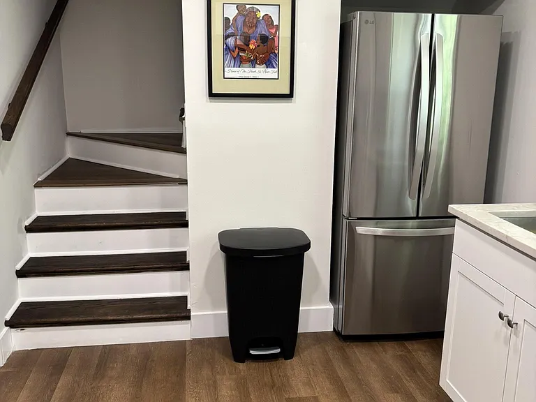 Kitchen area with stainless refrigerator, shaker cabinetry, and durable flooring near the stairwell for easy access.