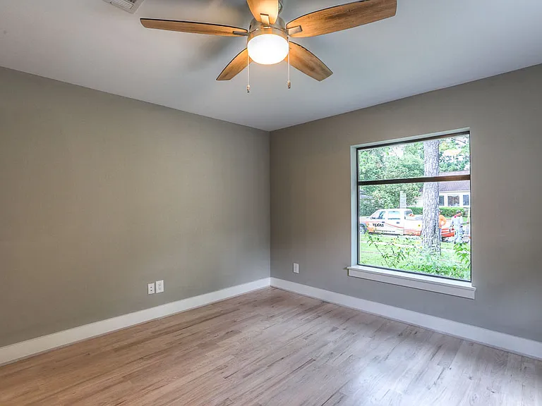Generously sized bedroom with hardwood floors, ceiling fan, and a large picture window with landscape and foliage views