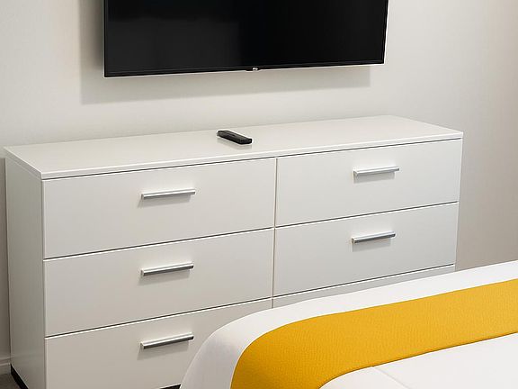 Bright and cozy bedroom with a wall-mounted TV and modern white dresser, offering a comfortable and relaxing space.