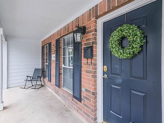 Large front porch with brick elevation, white pillars and shutters