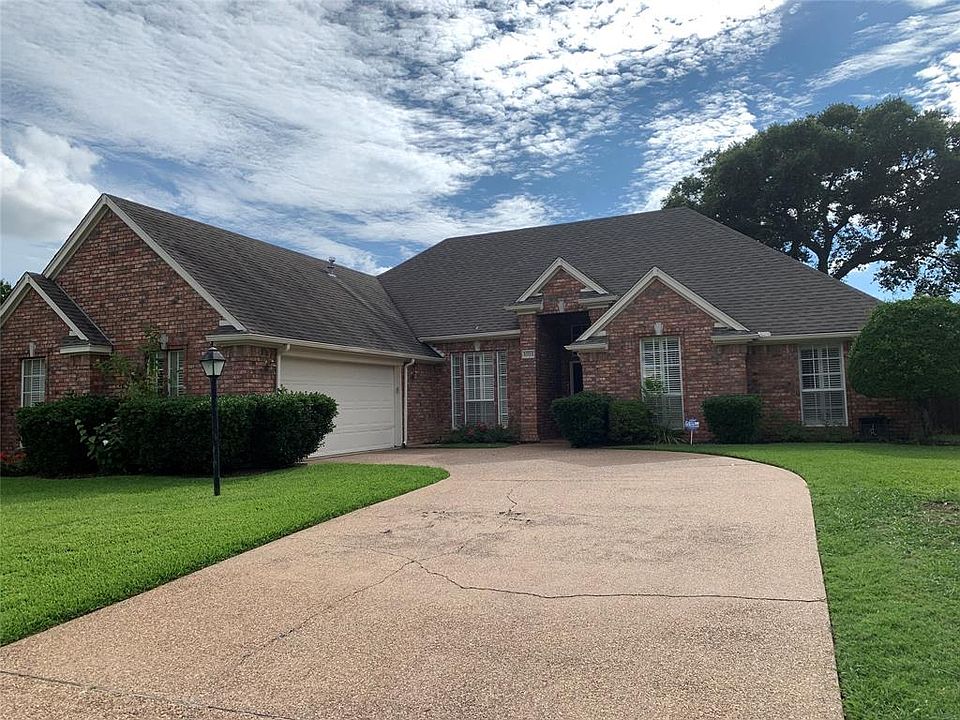 Traditional home featuring brick siding, driveway, roof with shingles, and a front lawn