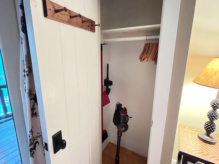 Closet with vacuum, mop, broom, and clothing storage options.