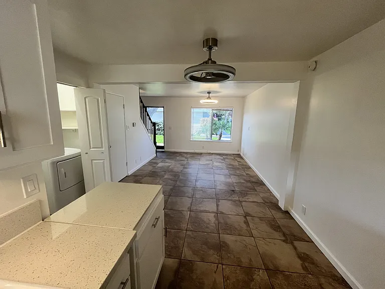 picture from the kitchen into the living room. 2 ceiling fan/lights. Stone look flooring through out first floor. Window overlooks green belt. Screen door on entrance and patio door. Laundry closet. Nice white paint throughout.