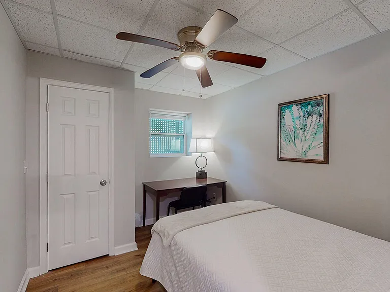 Furnished bedroom with ceiling fan, closet, window for natural light, and a dedicated desk area for work or study.
