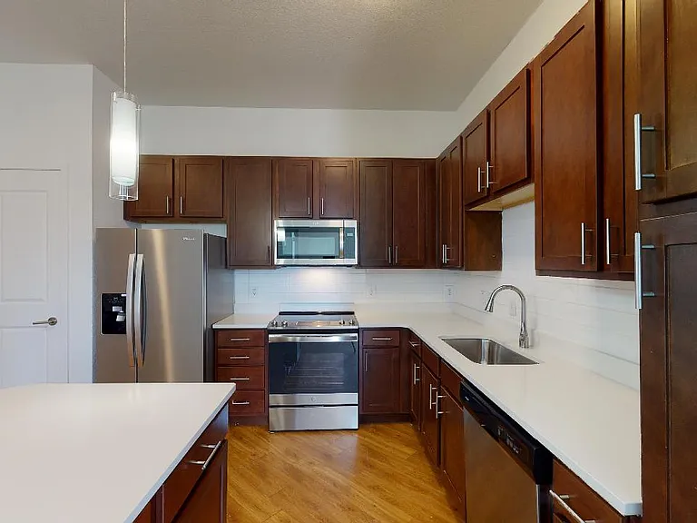 Apartment kitchen with stainless steel appliances, quartz countertops and wood-style flooring.
