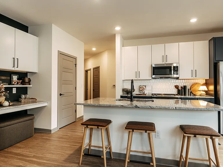 Contemporary apartment kitchen featuring granite countertops, stainless steel appliances, island seating, and a built-in bar area.