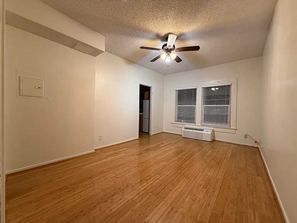 Living area with wood floors, tall ceilings, cooling fan, AC/heater unit, and bright windows.
