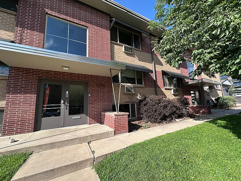 Charming brick apartment building with large windows, lush green lawn, and inviting entranceway, perfect for modern living.