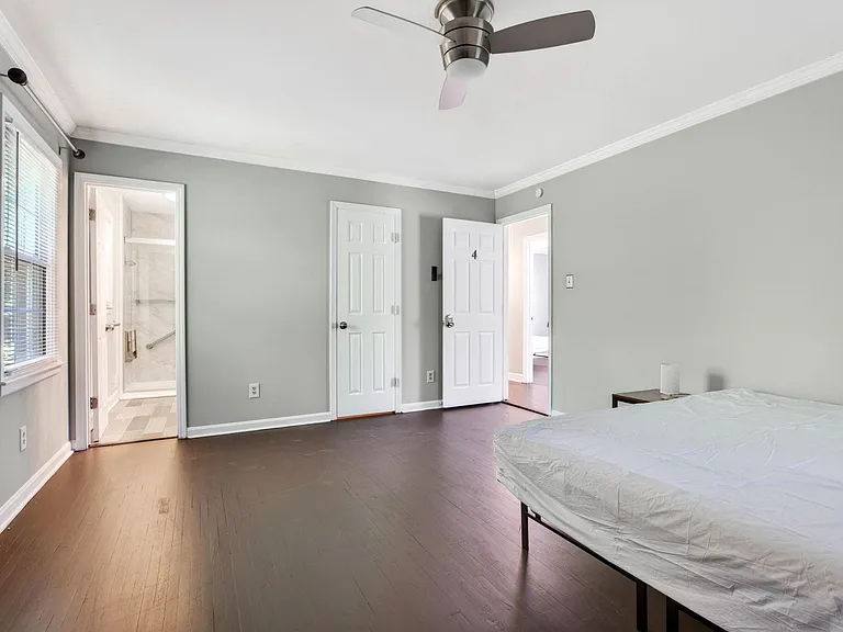 Spacious bedroom with hardwood floors, ceiling fan, and convenient access to an adjoining bathroom and hallway.