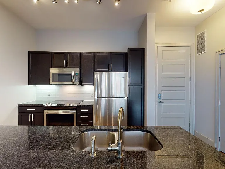 Apartment kitchen with stainless steel appliances, granite countertops and wood-style flooring.