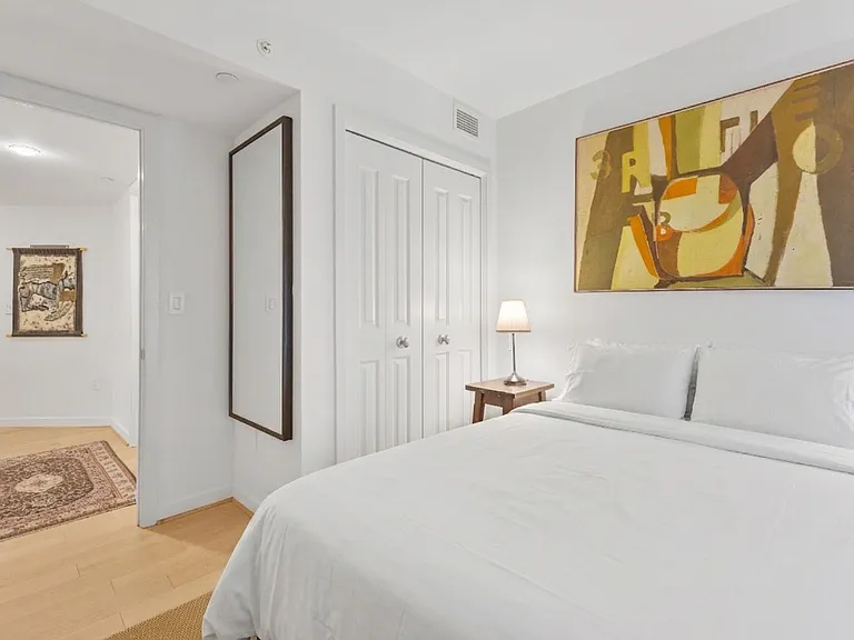 A bright, minimalist retreat offering ample closet space, a full-length mirror, and cozy bedside lighting.