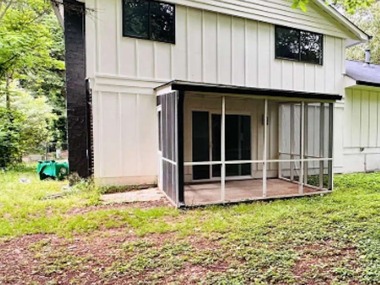 A dedicated screened-in patio and sliding glass doors, set on a spacious grassy yard with mature trees.