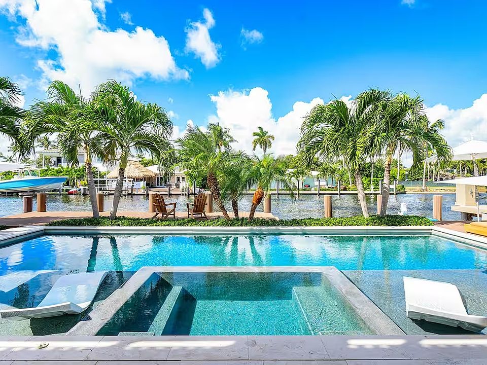 Luxury resort-style pool with Baja deck, lush palms, and chic lounge seating.