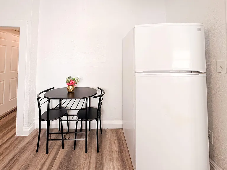 Compact dining nook with a two-seat cafe table set beside a full-size refrigerator, offering an easy spot for meals.
