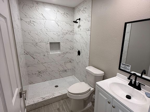 Updated bathroom with a walk-in tiled shower, niche shelving, and a vanity with under-sink storage and matte-black fixtures.