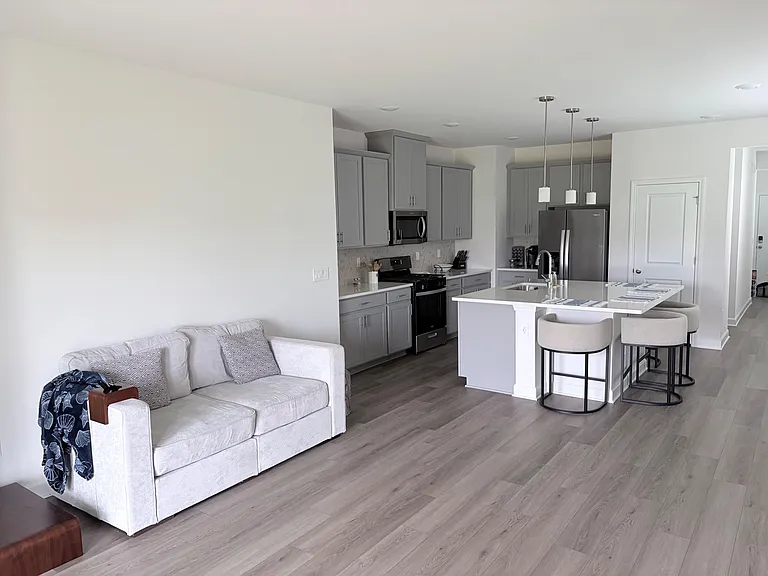 Open-concept kitchen with large island seating, gray cabinetry, and stainless steel appliances flowing into the living area.