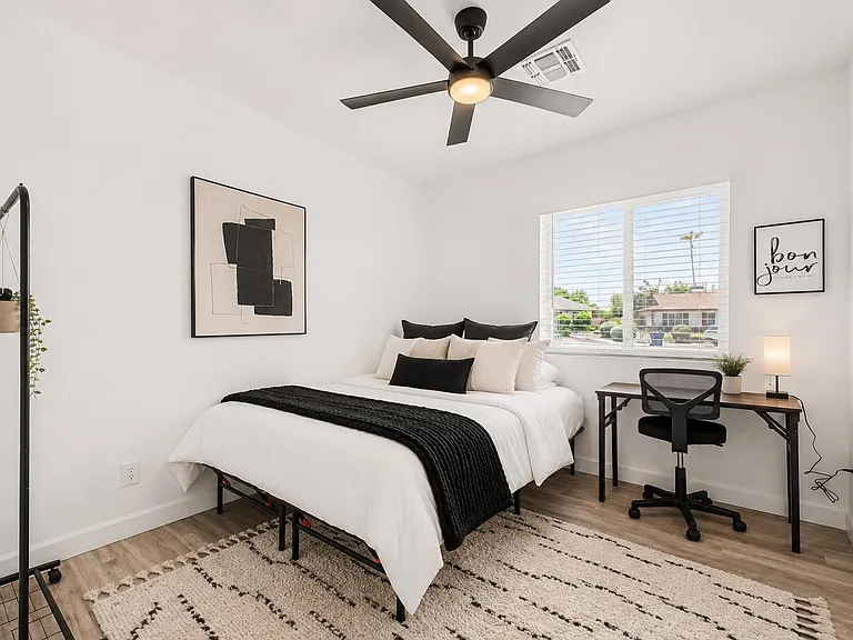 Well-appointed bedroom with a ceiling fan, large window with blinds, and a dedicated desk area for work or study.