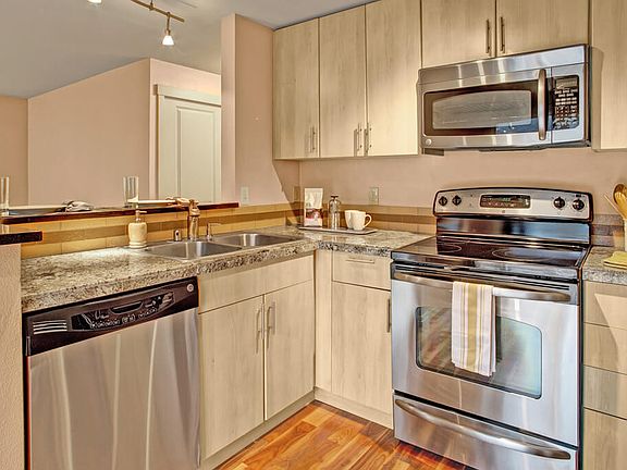 A kitchen with stainless steel appliances, stone countertaps, a small breakfast bar, and lots of cabinet space