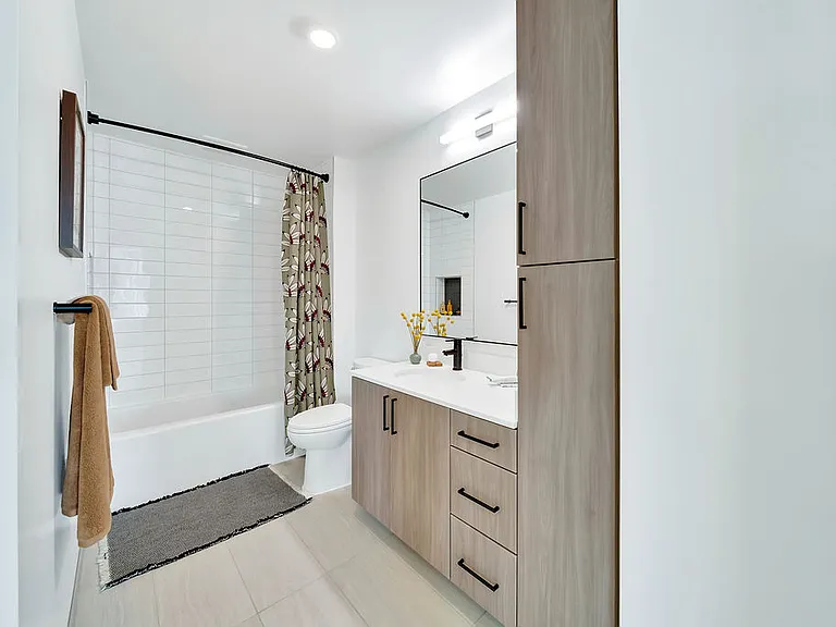 Modern bathroom with white walls, light wood cabinetry, large window, and decorative accents.