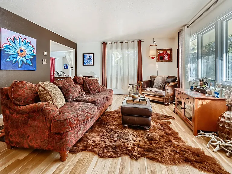 Large living room adorned with fine art and furnishings, large windows looking to the mountains and garden area.