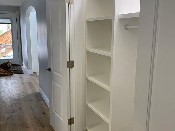 Hallway closet with built-in shelving, located opposite the bathroom. Front door seen in background. Includes full-view glass door with blinds for privacy.