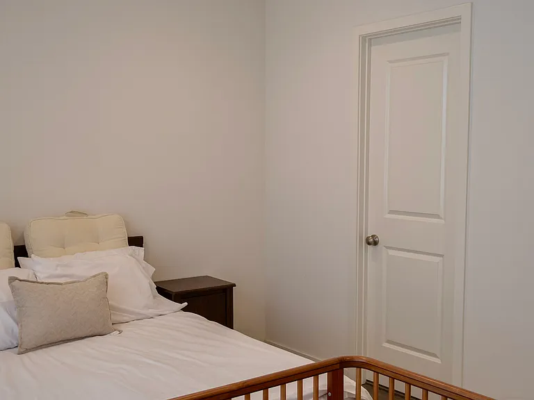 Primary Bedroom: Corner view highlighting the opposite side of the bed, showing the closed door leading to the en-suite bathroom.