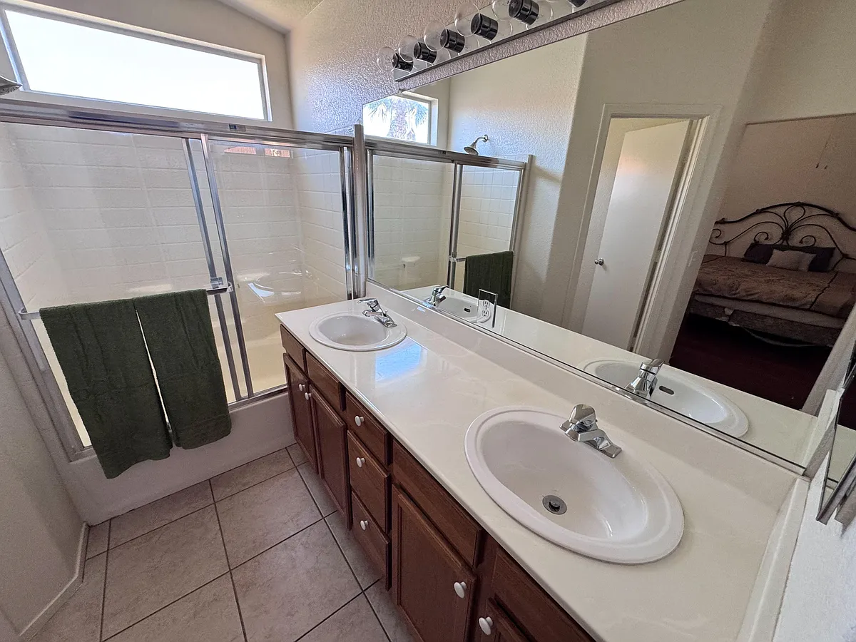 Bathroom with a double-sink vanity, large mirror, and a shower/tub combo with sliding glass doors and high windows. - Fall Meadows Ave