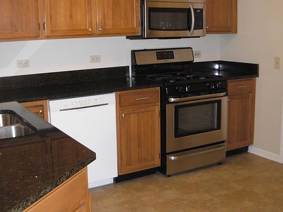 Kitchen has dishwasher, double sink, microwave, granite counters, gas stove, and refrigerator overlooking dining room and living room.