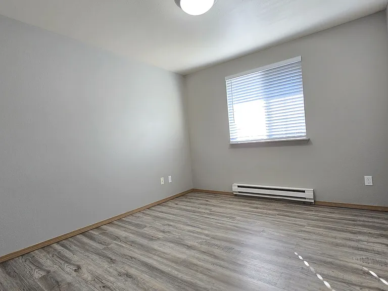 Bright and inviting guest bedroom with wood-style flooring, neutral finishes, and a sunlit window. Versatile layout offers the perfect space for guests, a home office, or additional living space.