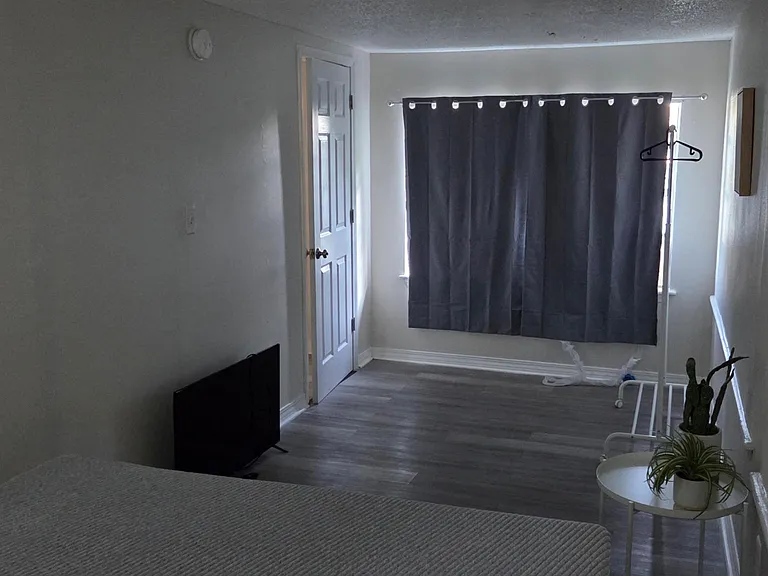 Private bedroom with wood-style flooring, a window with curtains, and space for a bed and small seating or storage.