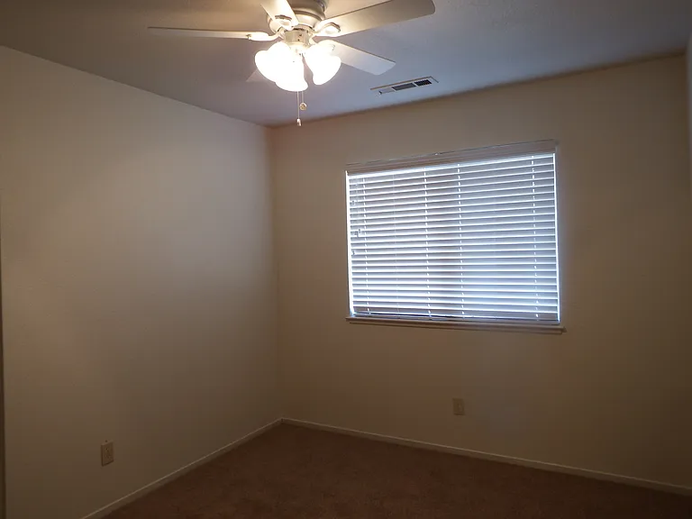 2nd bedroom with large window, wood blinds and ceiling fan.
