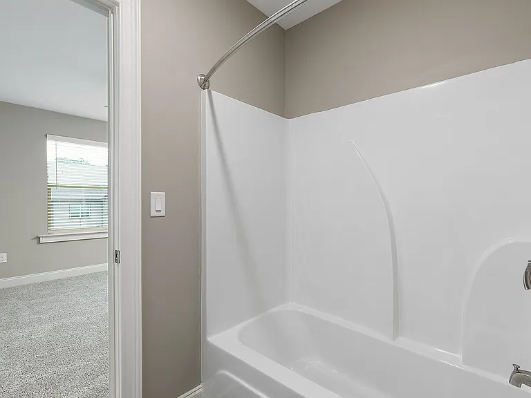 Bright and modern bathroom with elegant white bathtub and sleek fixtures, featuring a cozy adjoining carpeted bedroom with a large window.