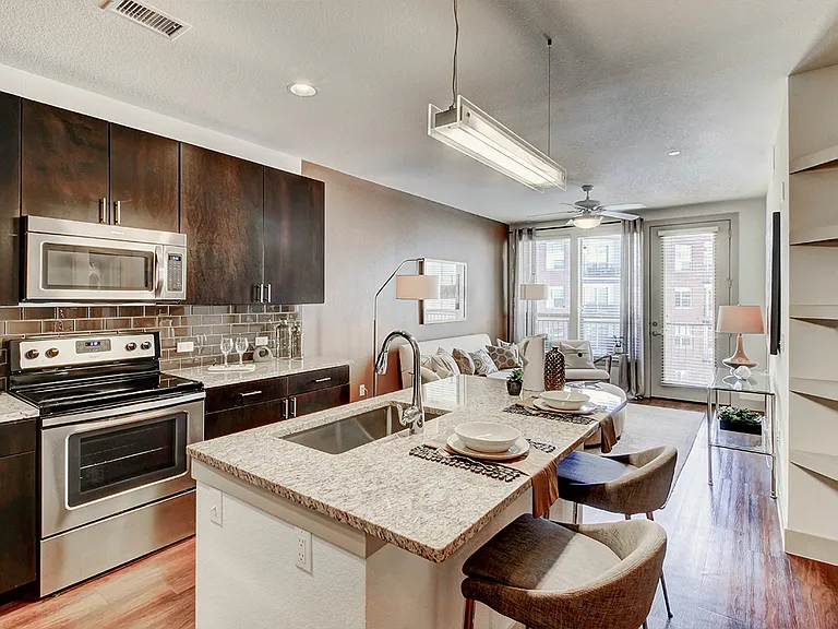 Apartment kitchen with stainless steel appliances, granite countertops and wood-style flooring.