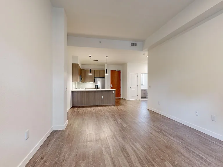 Apartment kitchen with stainless steel appliances, dining and living room with wood-style flooring.