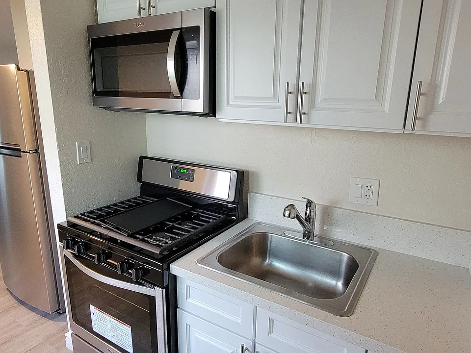 Kitchen with gas range, microwave and white cabinets at Orlando Woods Apartments in El Cajon, California.